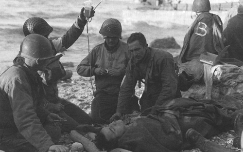 Photo:  Medics administering first aid to invasion casualties on OMAHA Beach