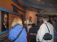 Photo:  An Army Corps of Engineers reenactor portraying Captain William Clark demonstrates the use of a sextant employed to determine one’s location to an audience at the Visitors Center/ Museum at the Lewis and Clark Historic Site.