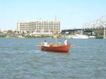 Photo: Red "Pirouge" approaching reviewing stand at Waterfront Park. This replica represents one of the two smaller vessels that accompanied the Keelboat.