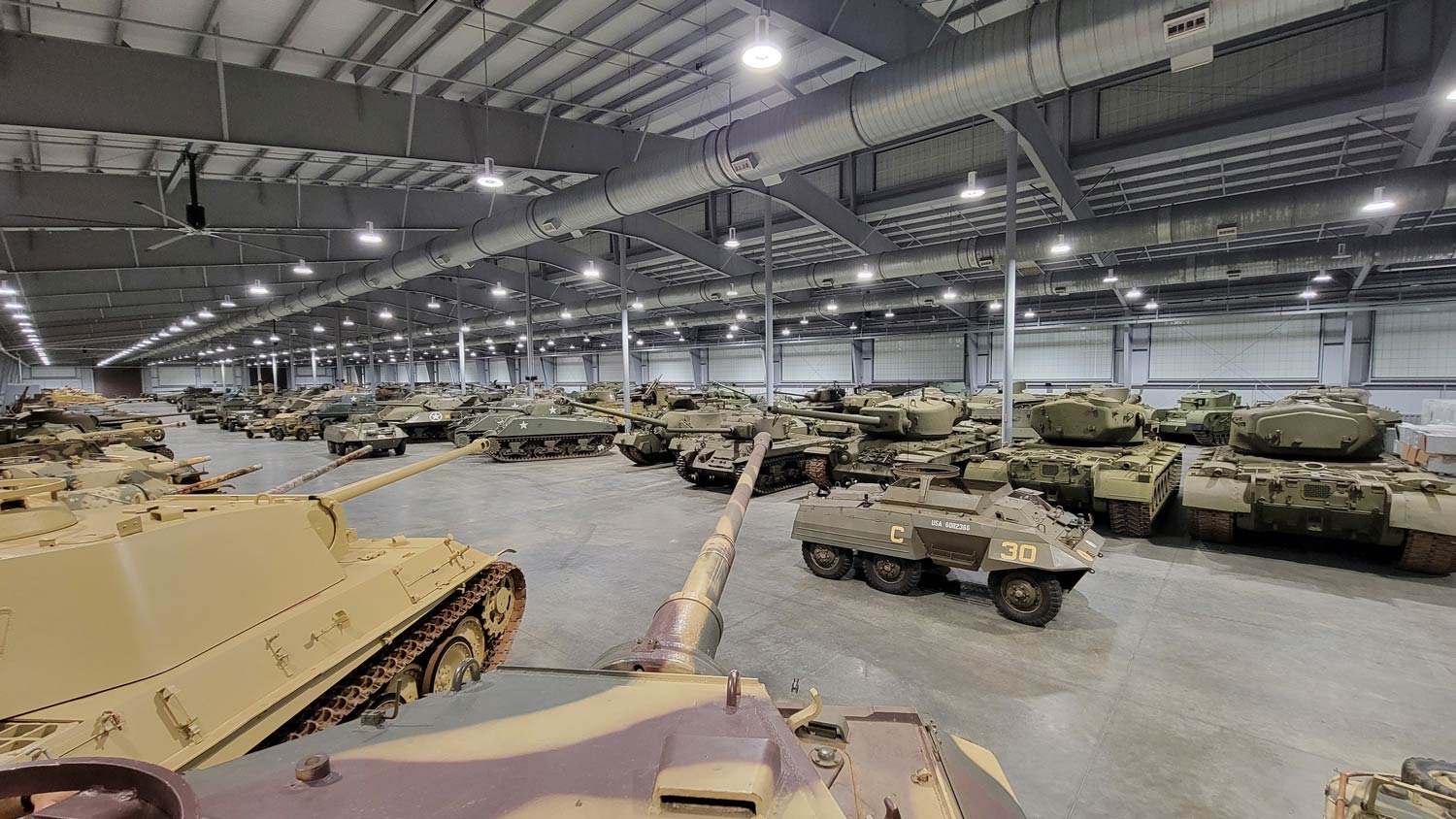 Many green and tan colored US Army tanks lined up in hangar.