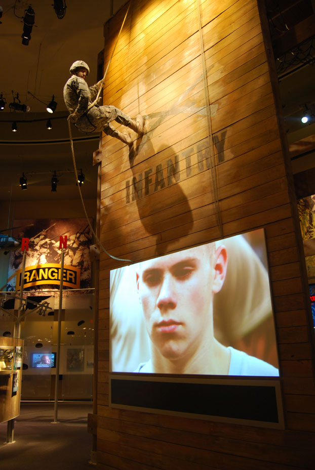 Museum display showing a video playing on a TV screen. Soldier is scaling a wall behind the screen.