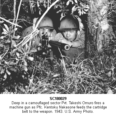 SC180029.  Deep in a camouflaged sector Pvt. Takeshi Omuro fires a machine gun as Pfc. Kentoku Nakasone feeds the cartridge belt to the weapon. 1943.  U.S. Army Photo.