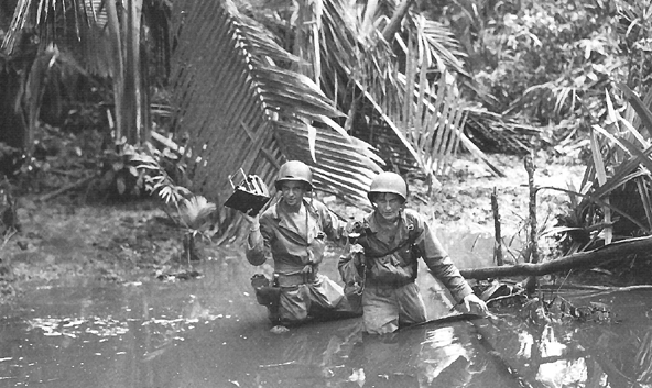 Photo:  Signal Corps cameramen wade through a stream during the invasion of New Guinea, April 1944
