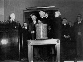 President Roosevelt, left, looks on as Secretary of War Stimson draws the first capsules in the National Lottery for selective service registrants in October 1940.