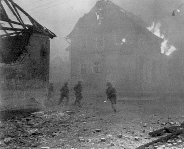 Infantrymen of the 6th Armored Division dash across an open street in a battle-torn German town.