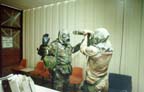 SSG Brian A. Craig (in MOPP-4) being checked for contamination at the Tactical Operations Center (TOC) military police desk before being allowed to enter the building
