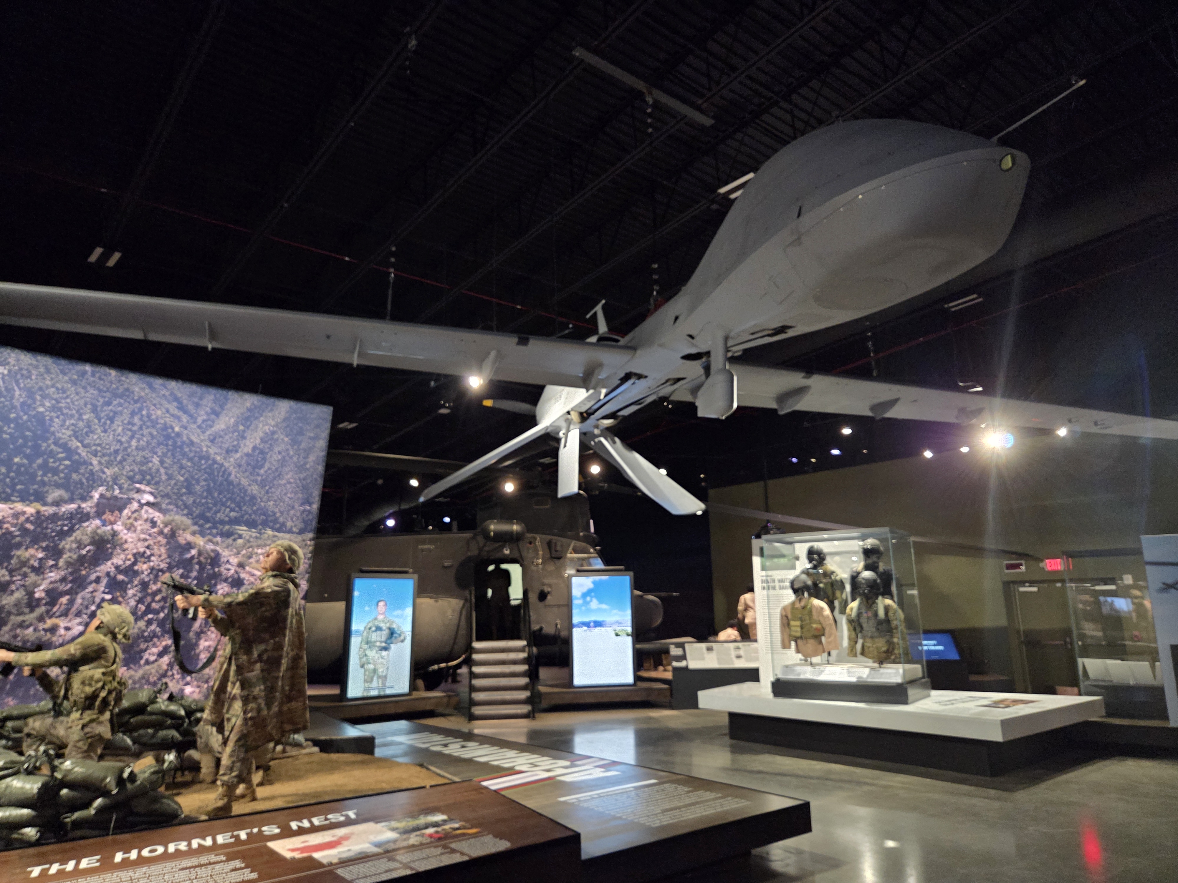 Museum gallery featuring a suspended MQ-1 Predator drone, helicopter display, and modern military exhibits.